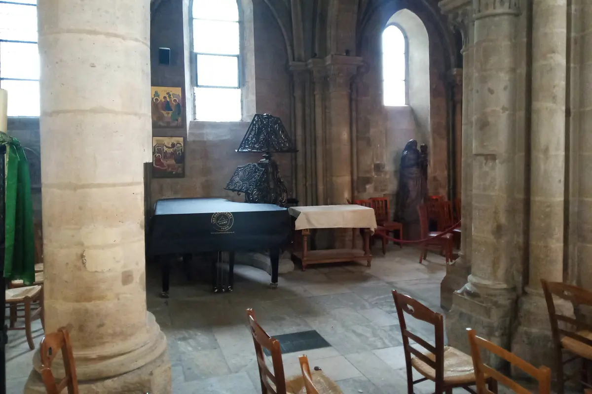 A grand piano and rows of wooden chairs beside a round Romanesque column inside Saint-Julien-le-Pauvre.