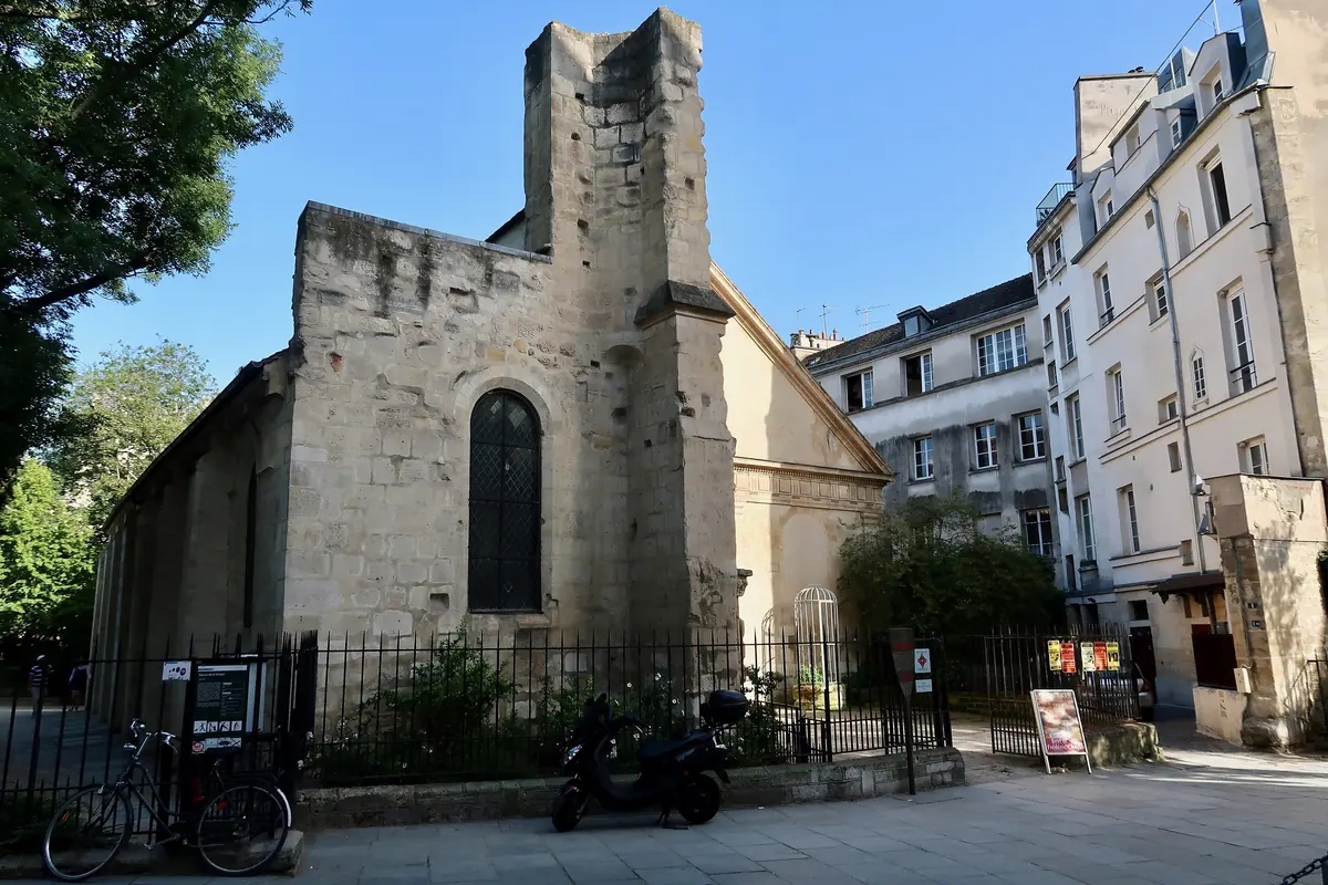 The cream stone west front and unfinished tower stump of Saint-Julien-le-Pauvre seen from the street, with Parisian apartment buildings beside it.