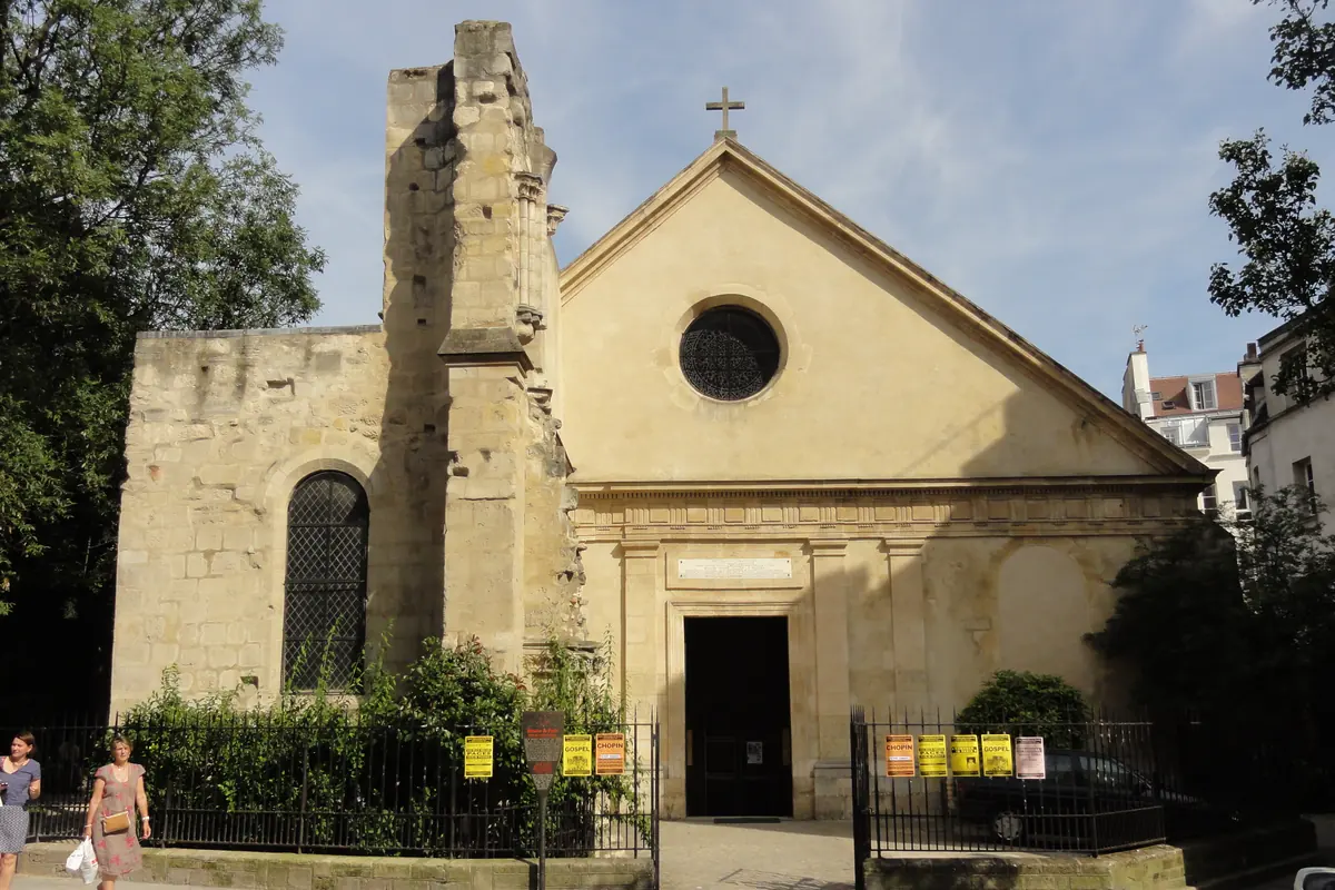 The plain cream west front of Saint-Julien-le-Pauvre with a round window above the door and the rough stump of an unfinished tower beside it.